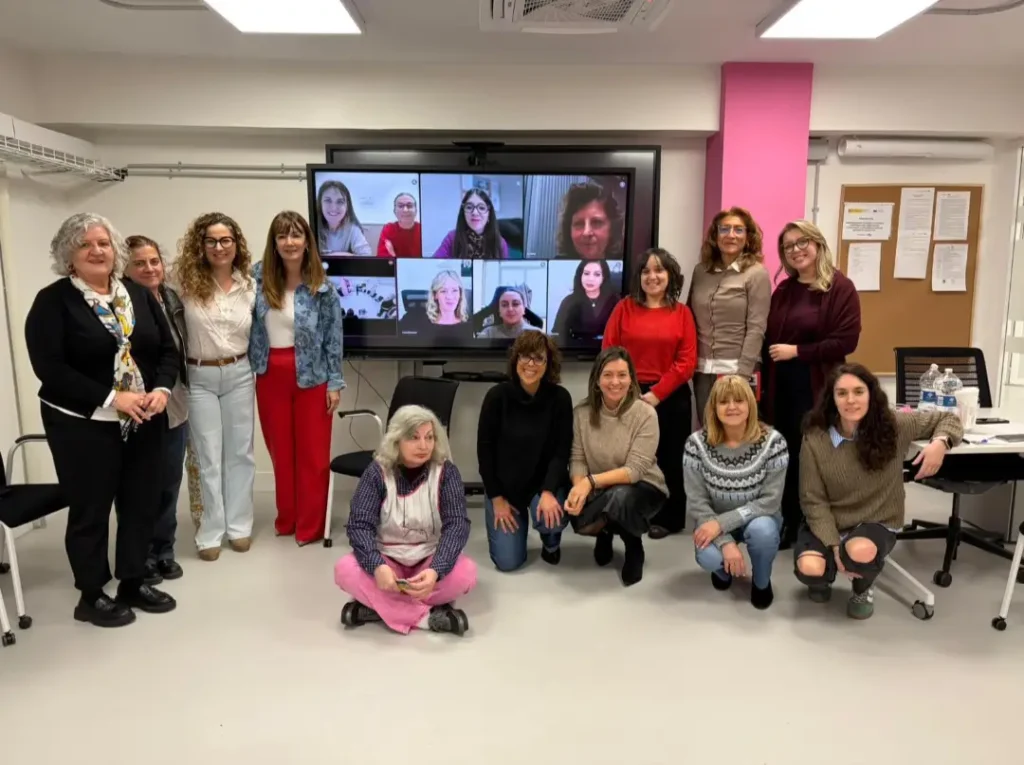 Natalia Salgado posa con un grupo de mujeres en una sesión de formación que combina asistencia presencial y participantes en remoto a través de pantalla.